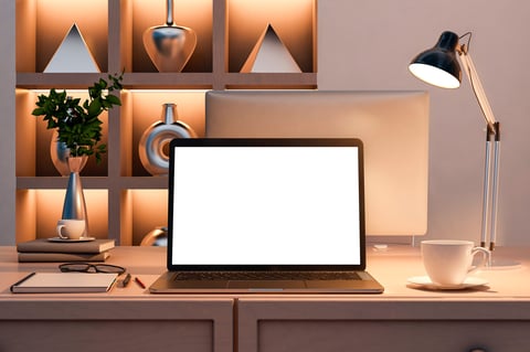 Laptop with blank screen on a clean desk, warm-lit shelves with decor in background.